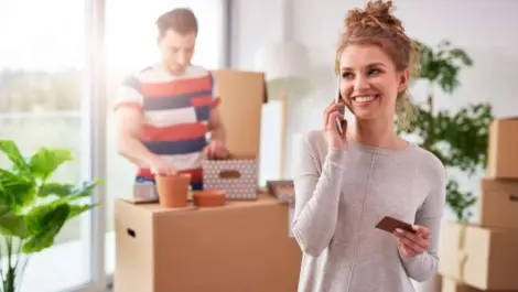 Woman on a cell phone while a man in the background opens a box